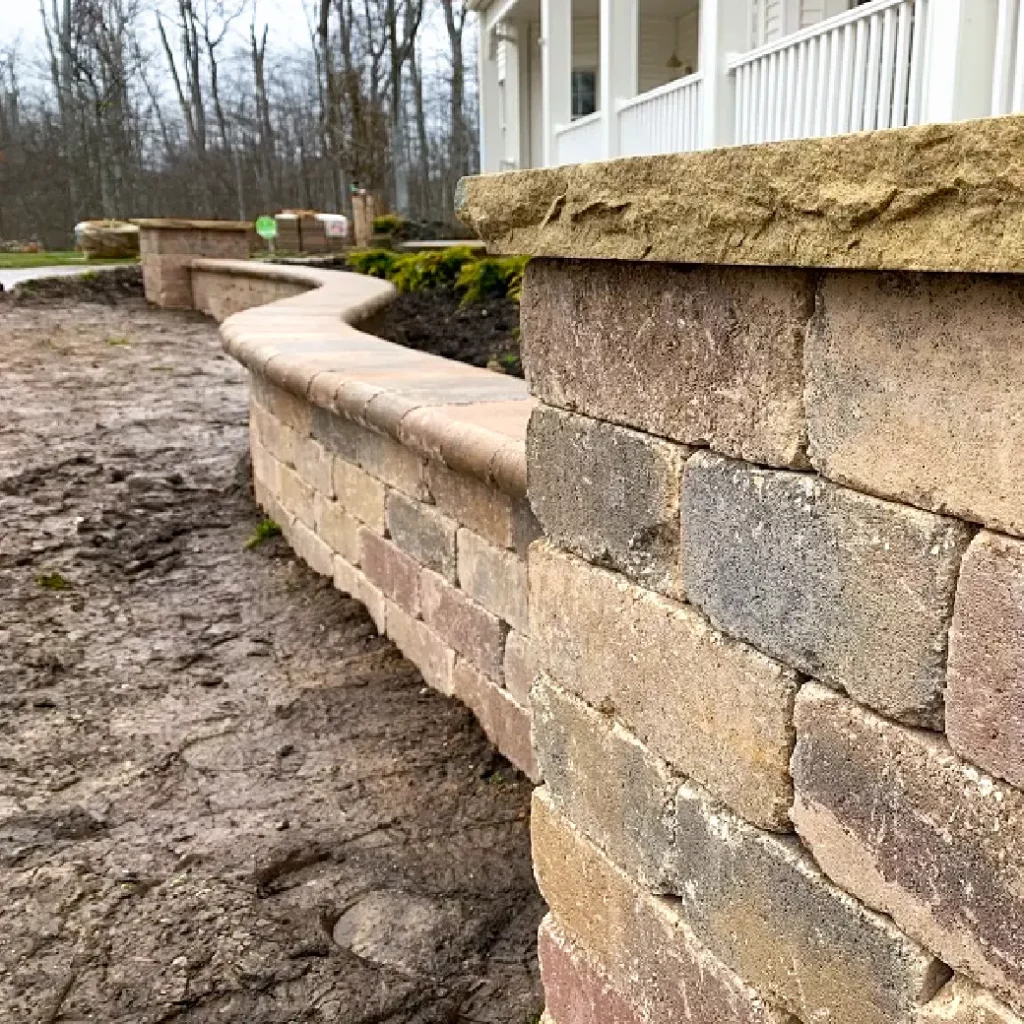 Curved block retaining wall construction with rough-cut rounded stone caps next to a residential home.