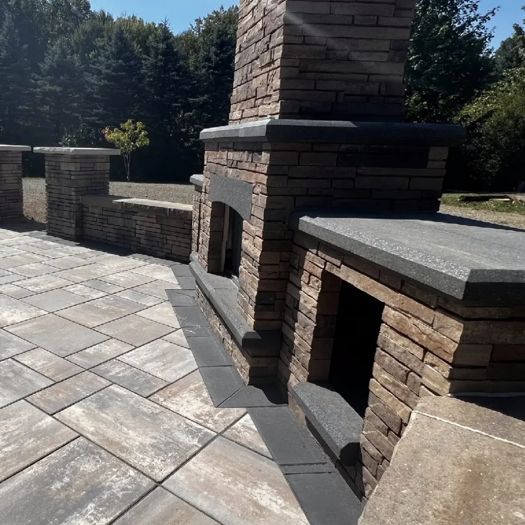 Outdoor fireplace and fire feature installation with stacked stone, granite caps, and built-in seating on a paver patio.