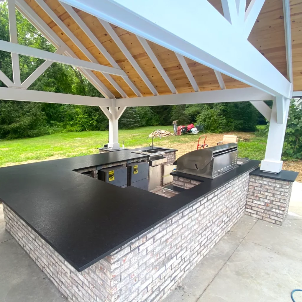 Outdoor kitchen near completion under a custom pergola featuring stainless grill and appliances.