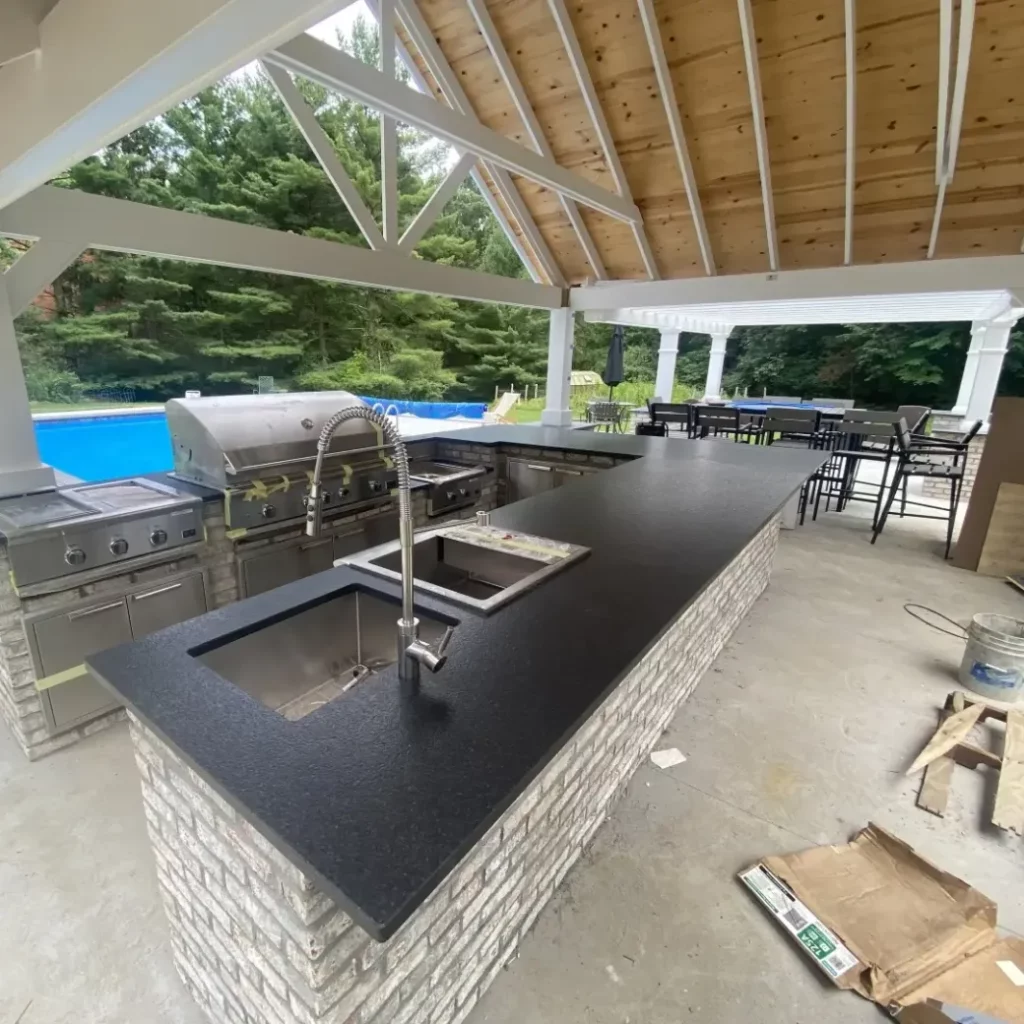 Outdoor kitchen installation with granite bar counter, stainless grill, bar sink, and poolside dining area.