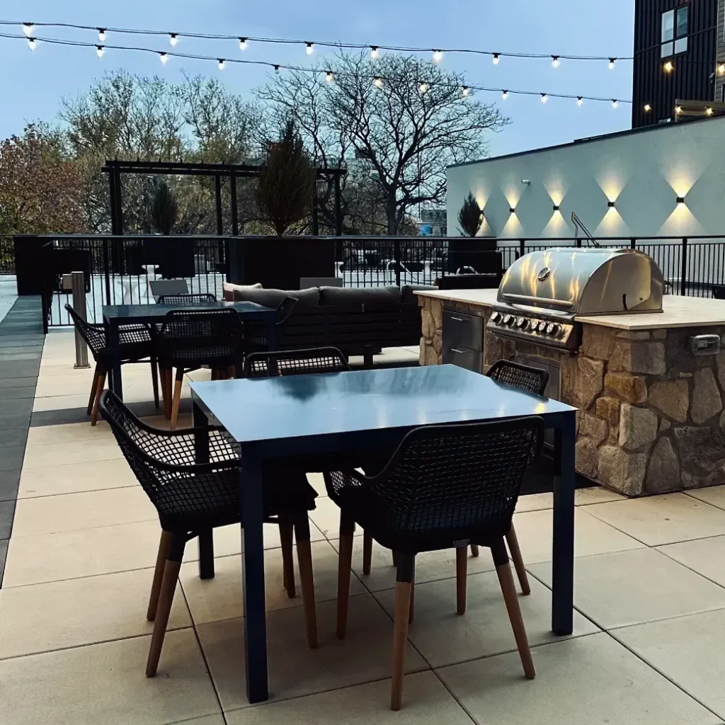 Paver patio outdoor living space with stone veneer grill station, dining area, and string lights.
