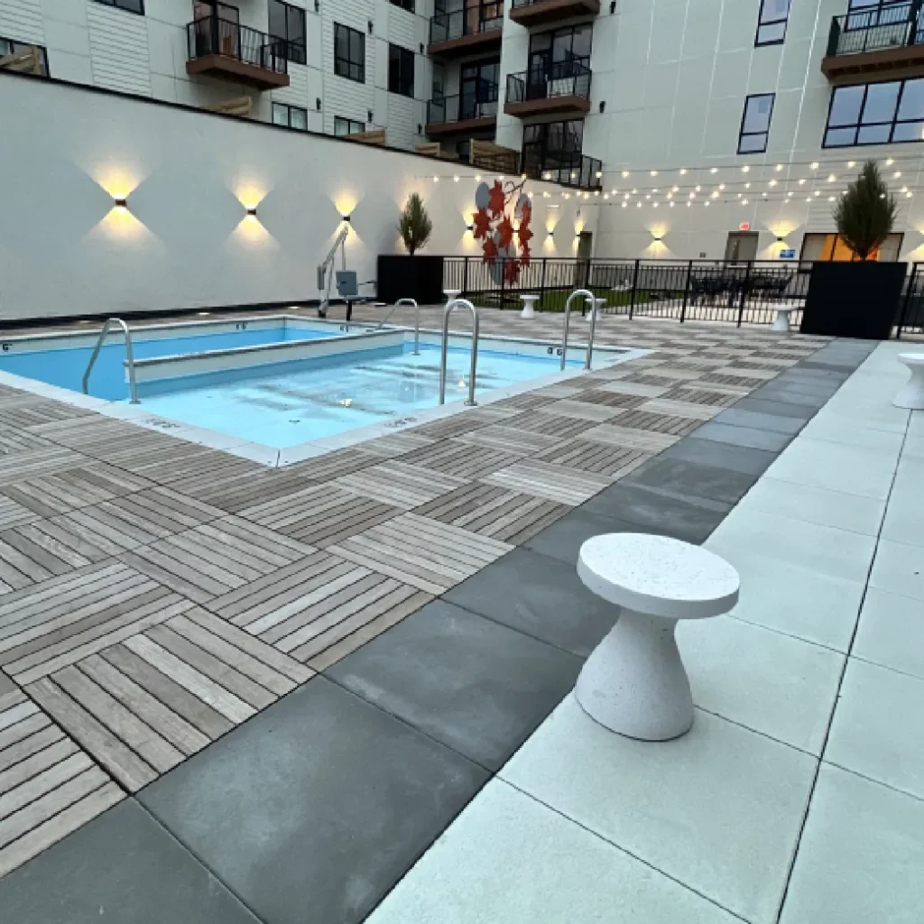 Outdoor living space courtyard patio with pool, wood tile deck, wall-mounted lighting, and string lights.