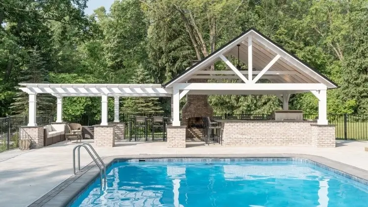 An outdoor pool with covered patio and outdoor kitchen, designed and constructed by Carmel Landscapes in Pepper Pike