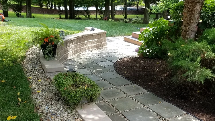 Stone walkway built with gray pavers in a residential backyard leading to patio.