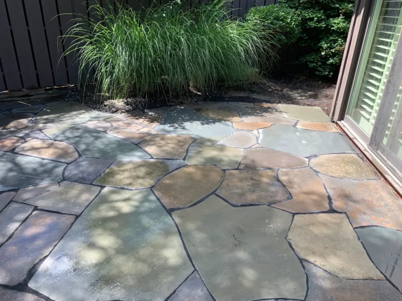 Natural cut stone creates a smooth patio with blue and brown stones in a residential backyard garden.