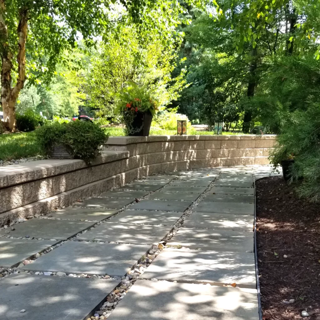 Retaining wall installation alongside a stone slab walkway with river rock joints and landscaped garden beds.