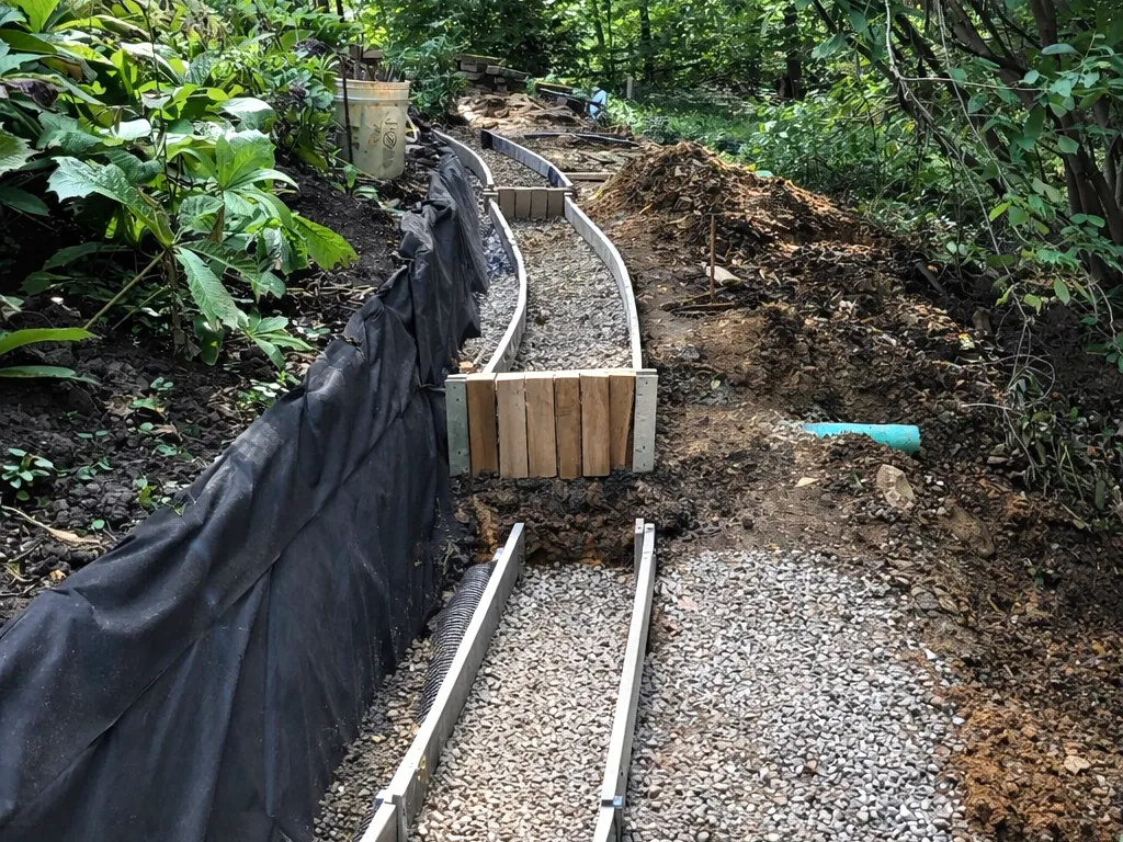 Retaining wall installation in progress in Chagrin Falls Ohio, showing gravel base, drainage fabric, and form work on a sloped residential property