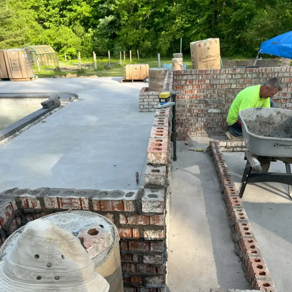 a mason works on patio construction in progress, poured concrete, brick masonry, green forest