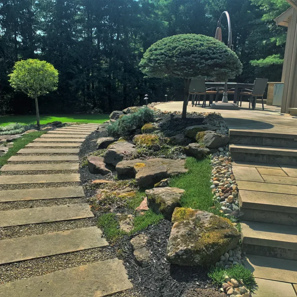 Stone patio installation with large slab walkway, stone steps, natural boulder garden, and manicured trees.